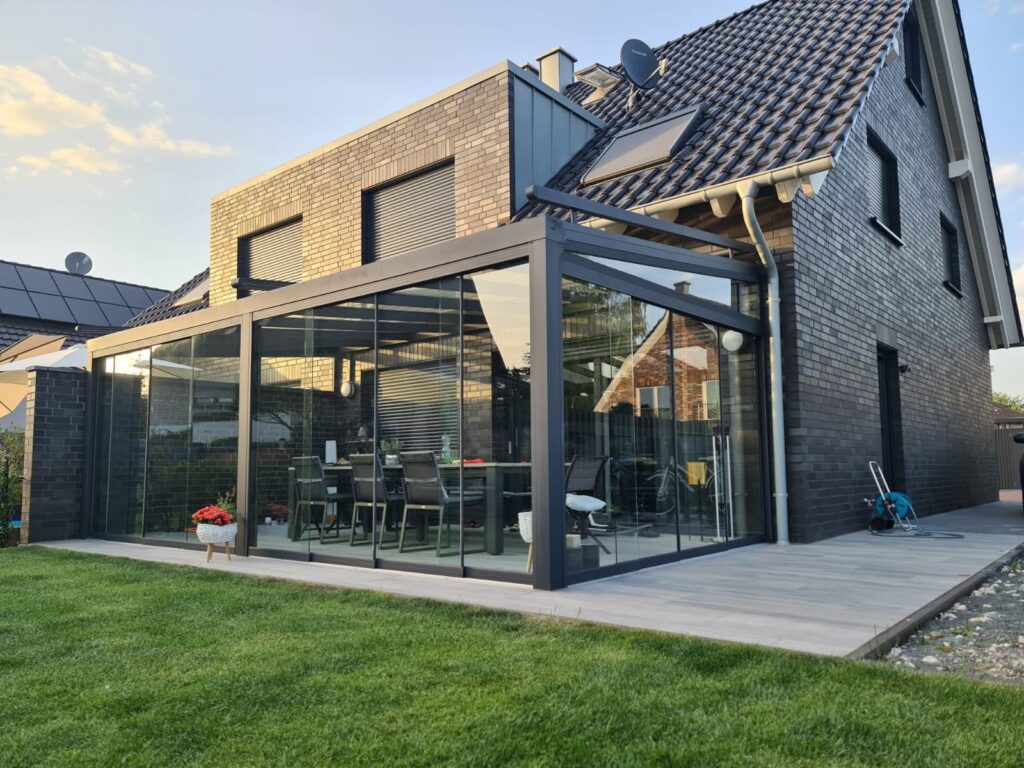 Terrassenüberdachung aus Aluminium mit Glasschiebewänden an modernem Einfamilienhaus