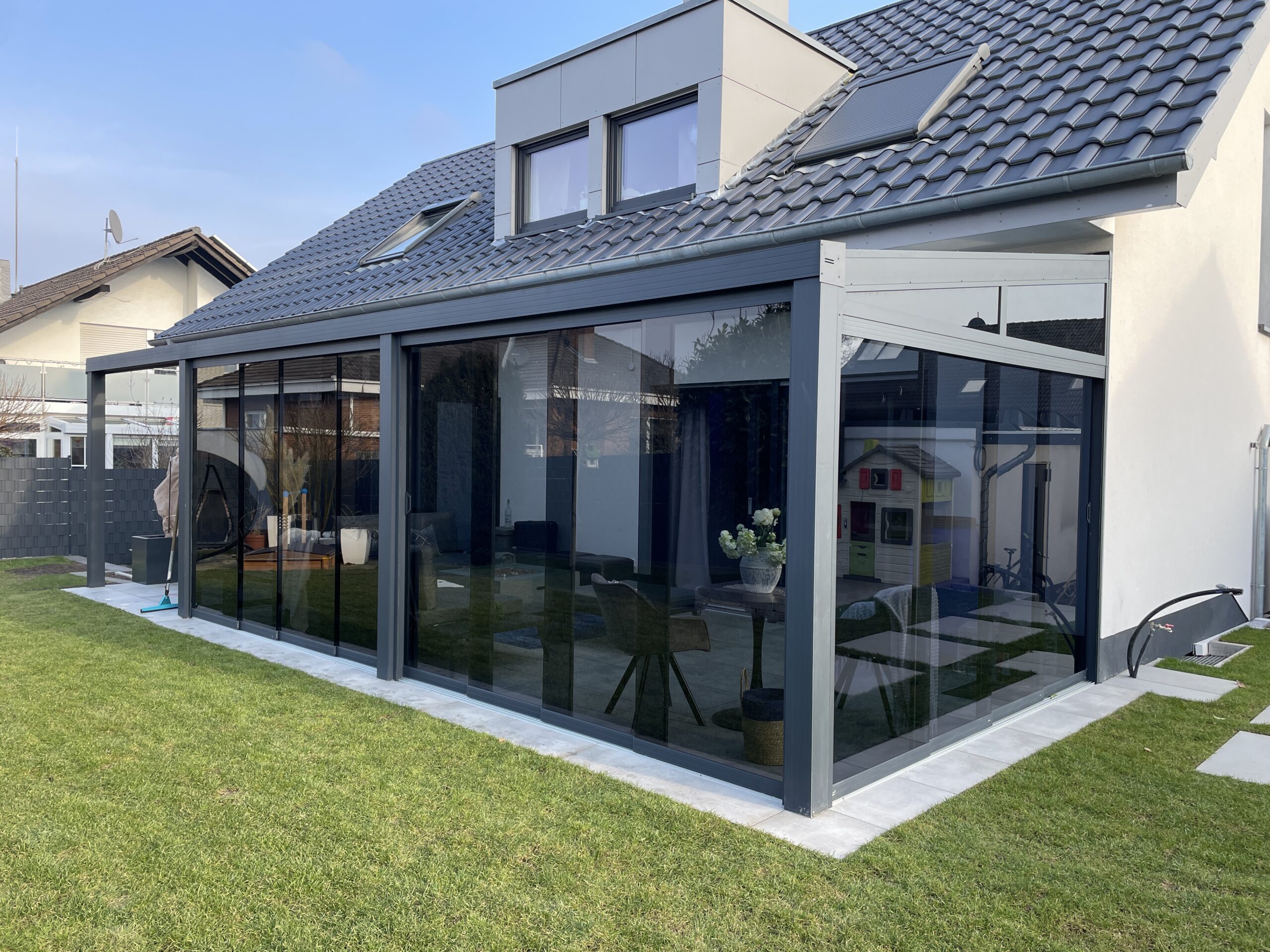 Terrassenüberdachung mit dunklen Glasschiebewänden an Einfamilienhaus