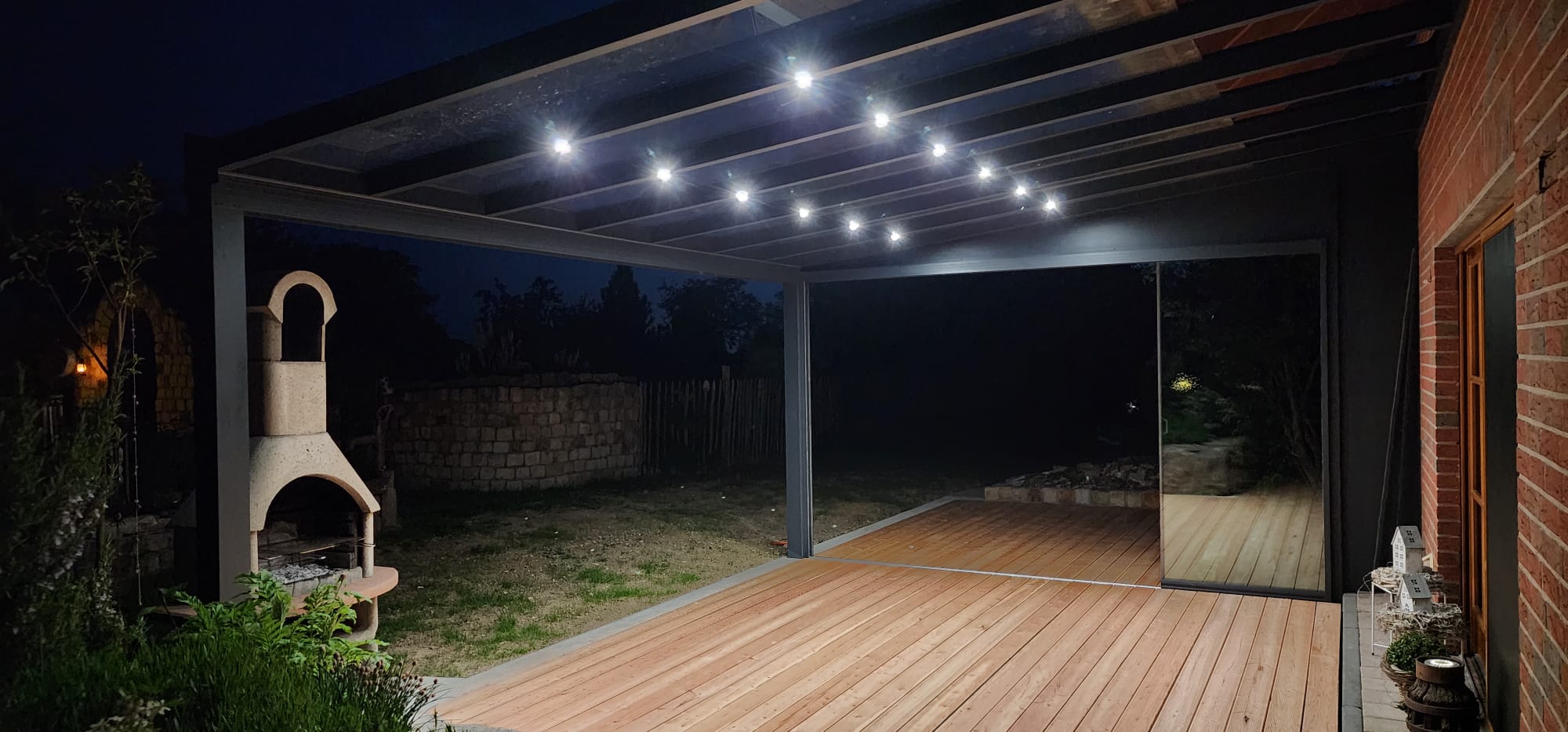 Terrassenüberdachung mit LED-Beleuchtung und Glasschiebewand bei Nacht