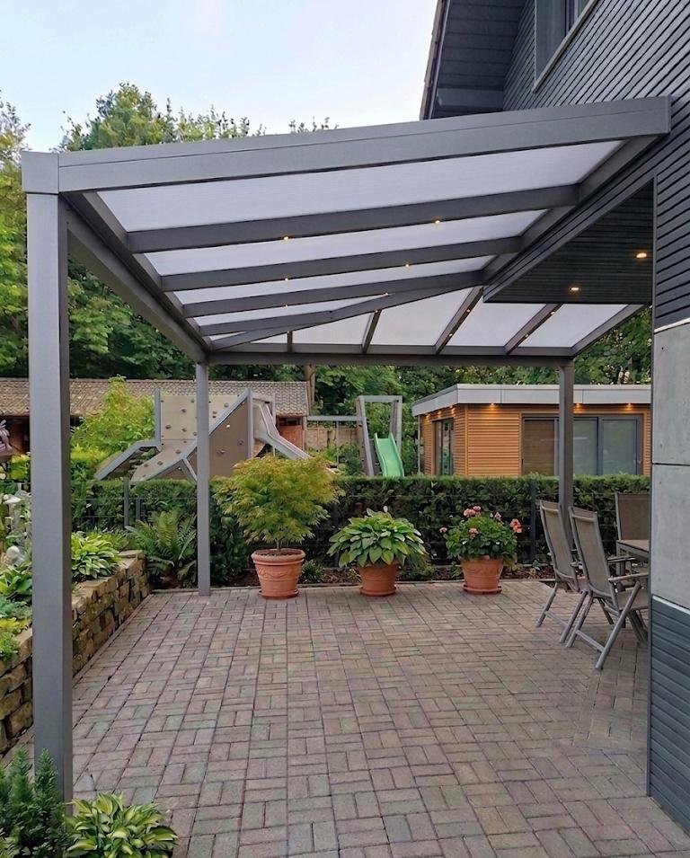 Terrassenüberdachung aus Aluminium mit leicht geneigtem Dach und integrierter Beleuchtung im Garten