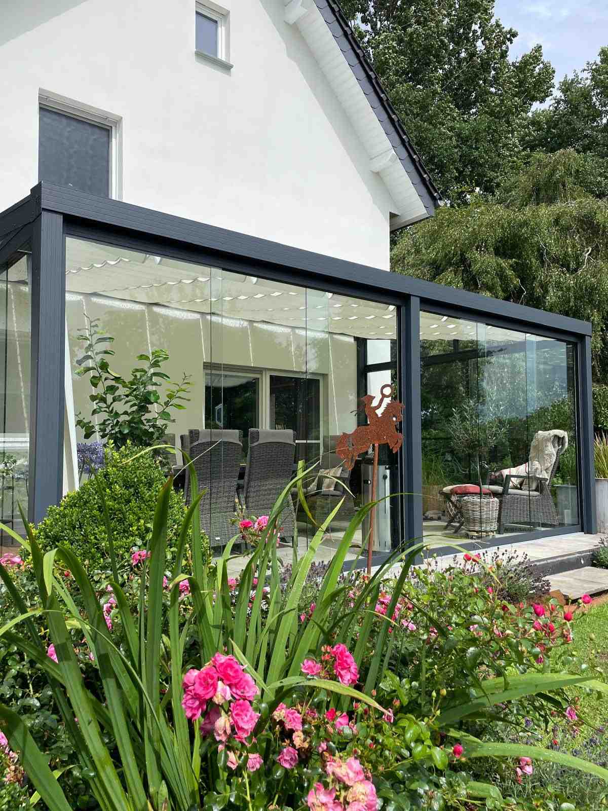 Terrassenüberdachung aus Aluminium mit Glasschiebewänden in einem gepflegten Garten