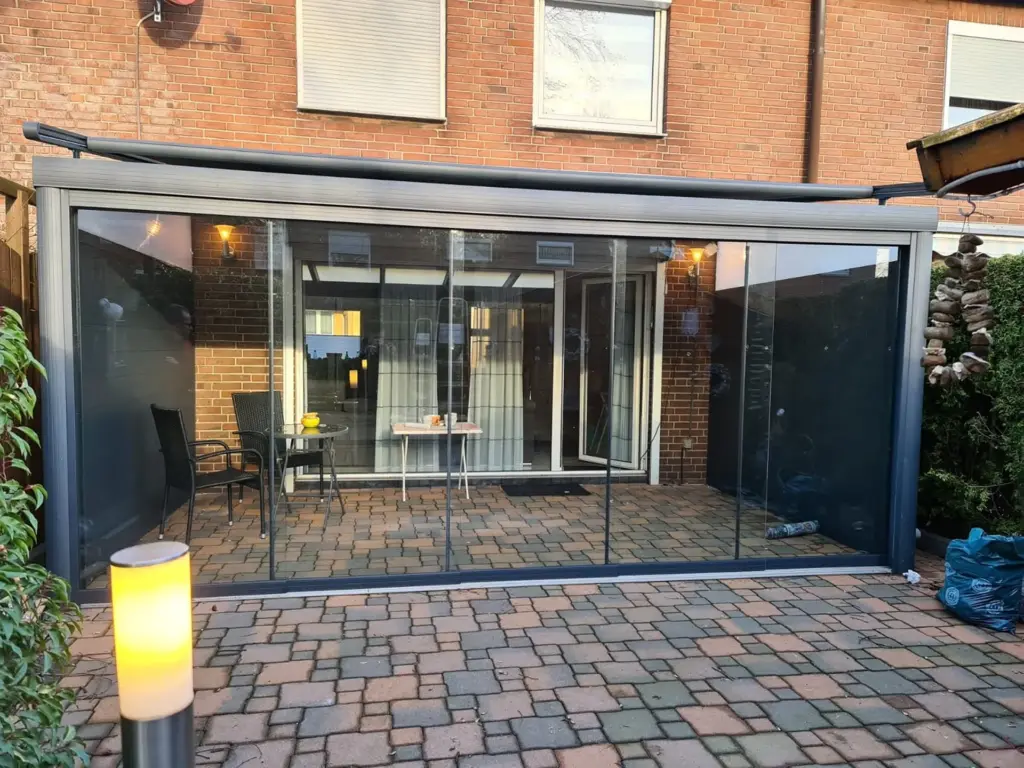 Kaltwintergarten mit Glasschiebetüren und Aluminiumdach auf gepflasterter Terrasse