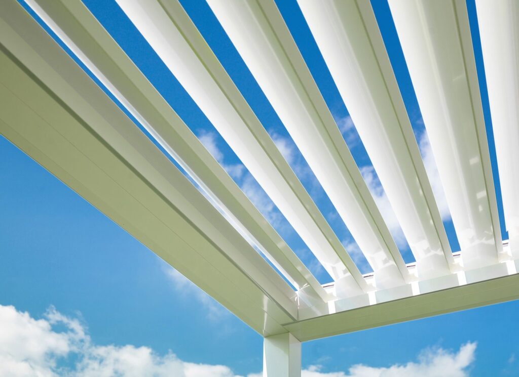 Detailansicht eines weißen Lamellendachs mit geöffneten Lamellen und Blick zum Himmel