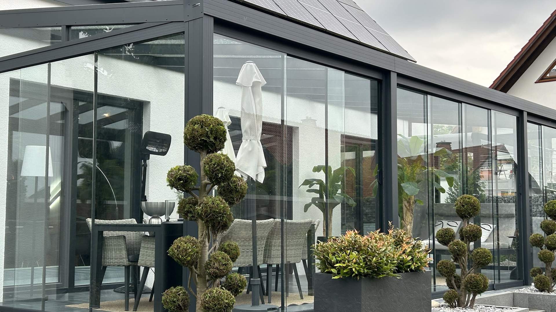 Terrassendach mit Glas-Schiebeanlagen an einem Wohnhaus mit moderner Gartengestaltung