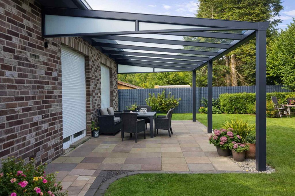 Große Aluminium-Terrassenüberdachung mit Glasdach und Sitzgruppe an Backsteinhaus