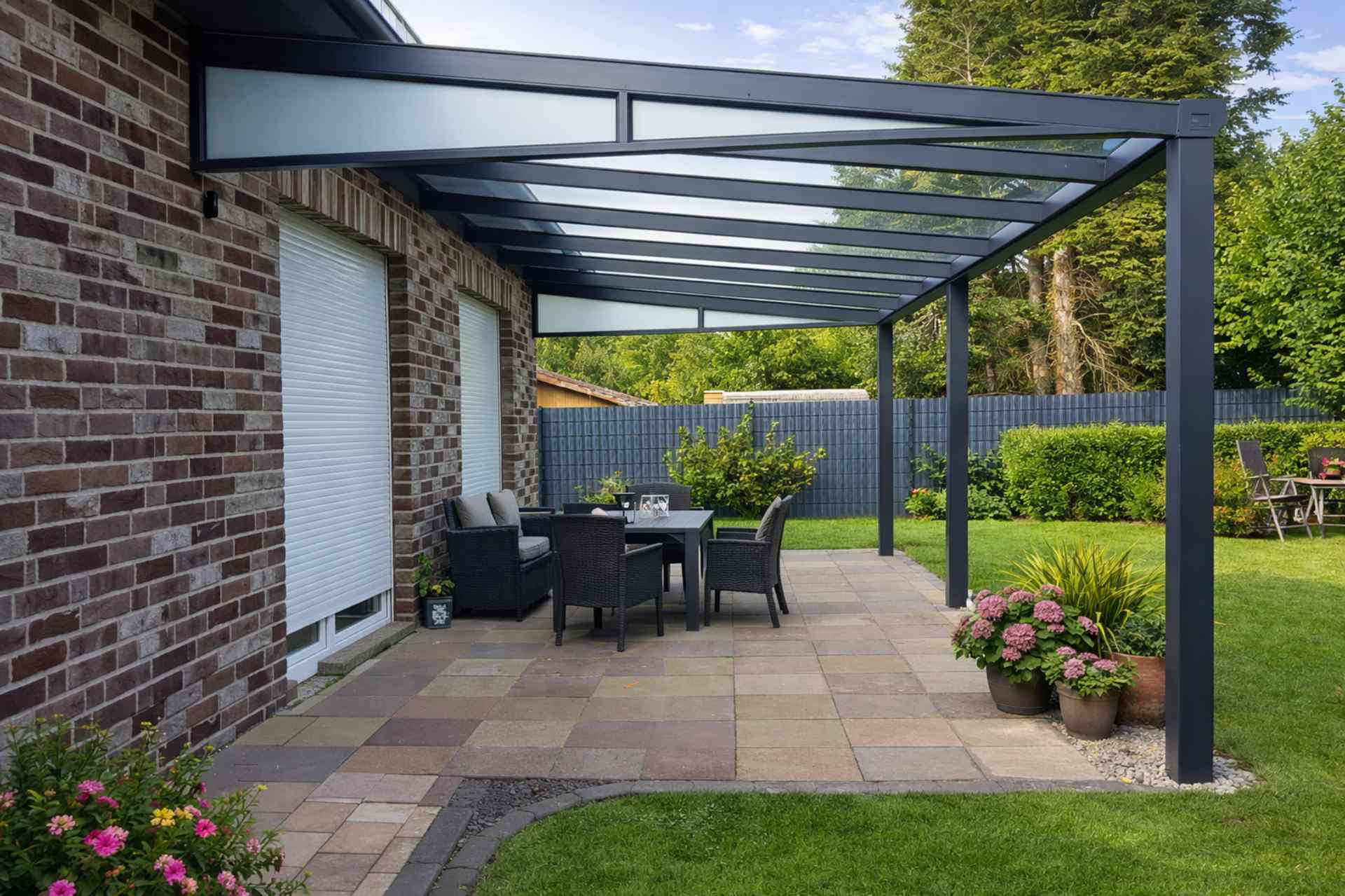 Große Aluminium-Terrassenüberdachung mit Glasdach und Sitzgruppe an Backsteinhaus