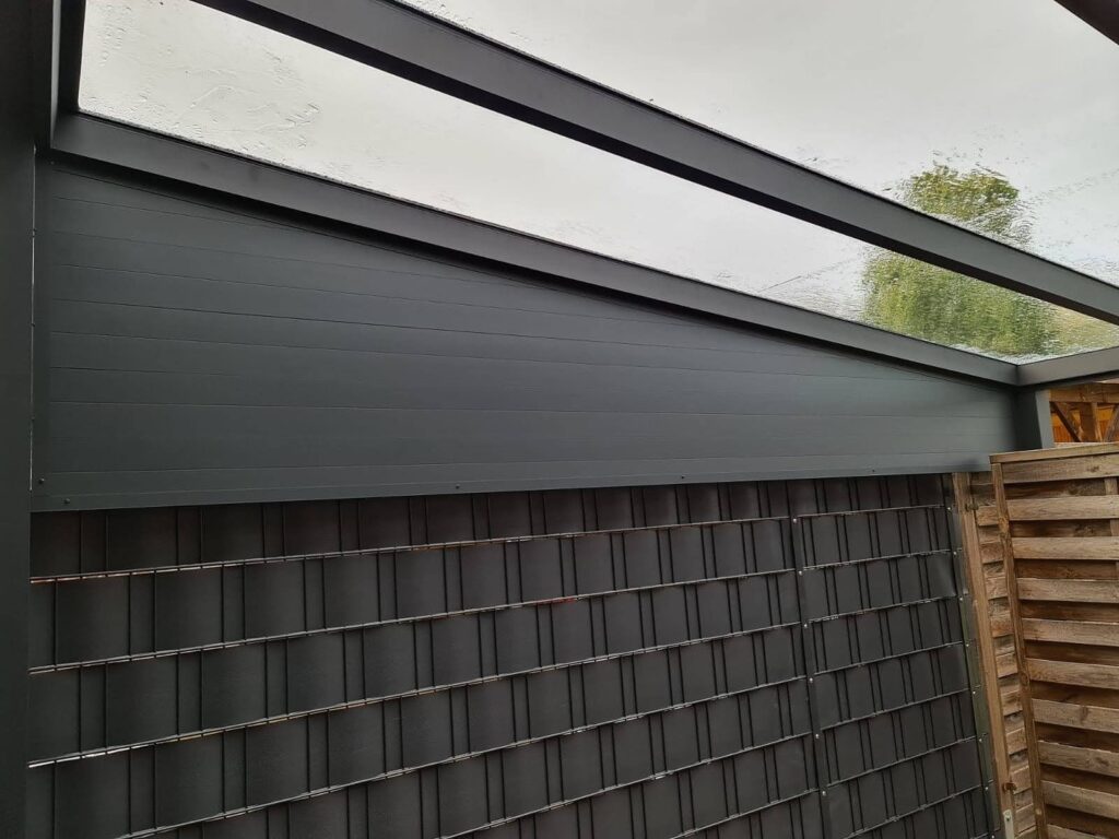 Detailansicht einer modernen Terrassenüberdachung mit geneigtem Glasdach und dunkler Aluminiumverkleidung