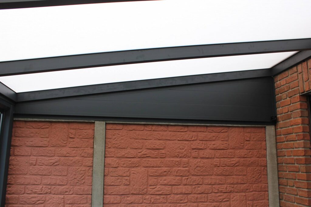 Detail einer Terrassenüberdachung mit geneigtem Glasdach und schwarzer Aluminiumblende an einer Ziegelwand