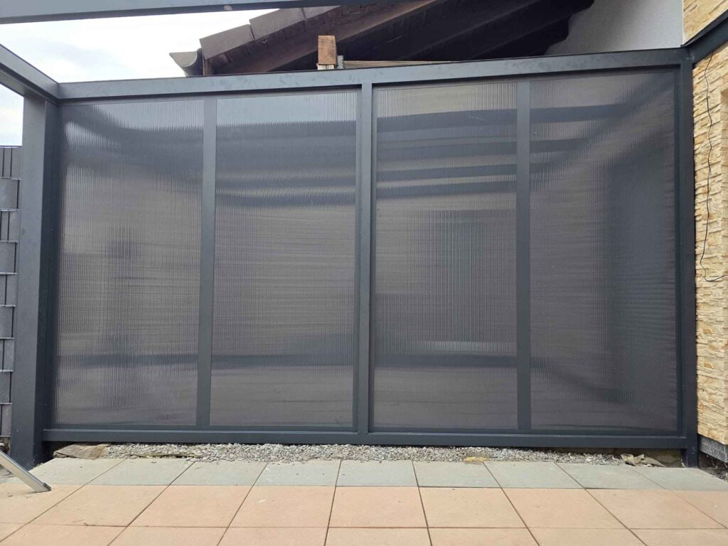 Seitenelement einer Terrassenüberdachung mit dunklem Aluminiumrahmen und strukturierten, blickdichten Paneelen