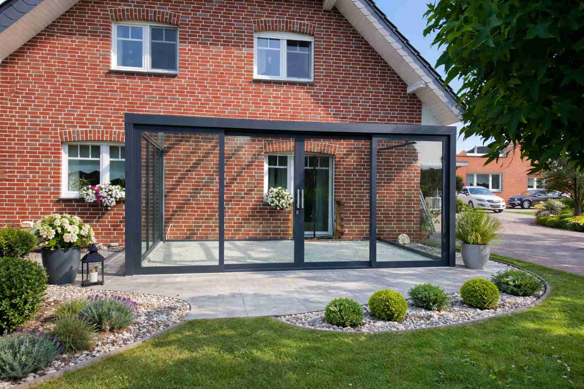 Moderne Terrassenüberdachung mit Glas-Schiebeelementen an einem Einfamilienhaus aus Backstein