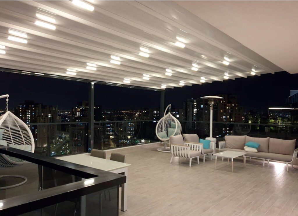 Moderne Dachterrasse mit beleuchteter Terrassenüberdachung bei Nacht und Blick auf die Stadt