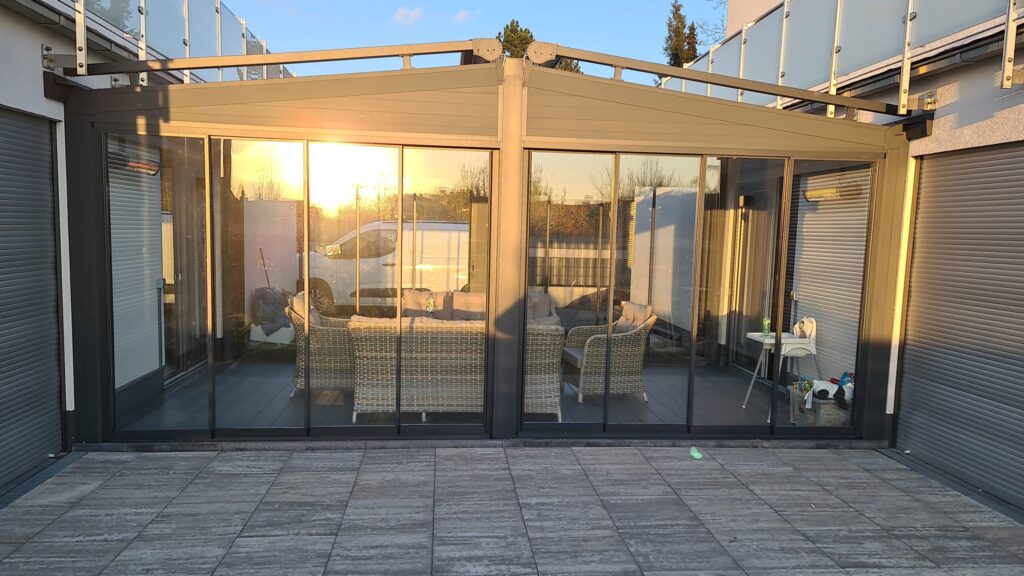 Terrassenüberdachung mit Glasschiebeanlage und Aluminiumrahmen bei Sonnenuntergang