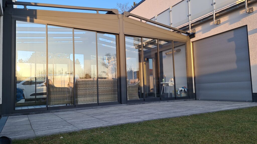 Terrassenüberdachung mit Glasschiebeanlage und Aluminiumrahmen bei Sonnenuntergang