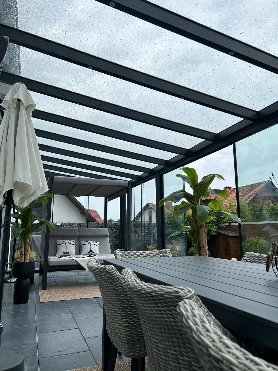 Überdachte Terrasse mit Glasdach, Schiebeelementsystem und stilvoller Outdoor-Einrichtung