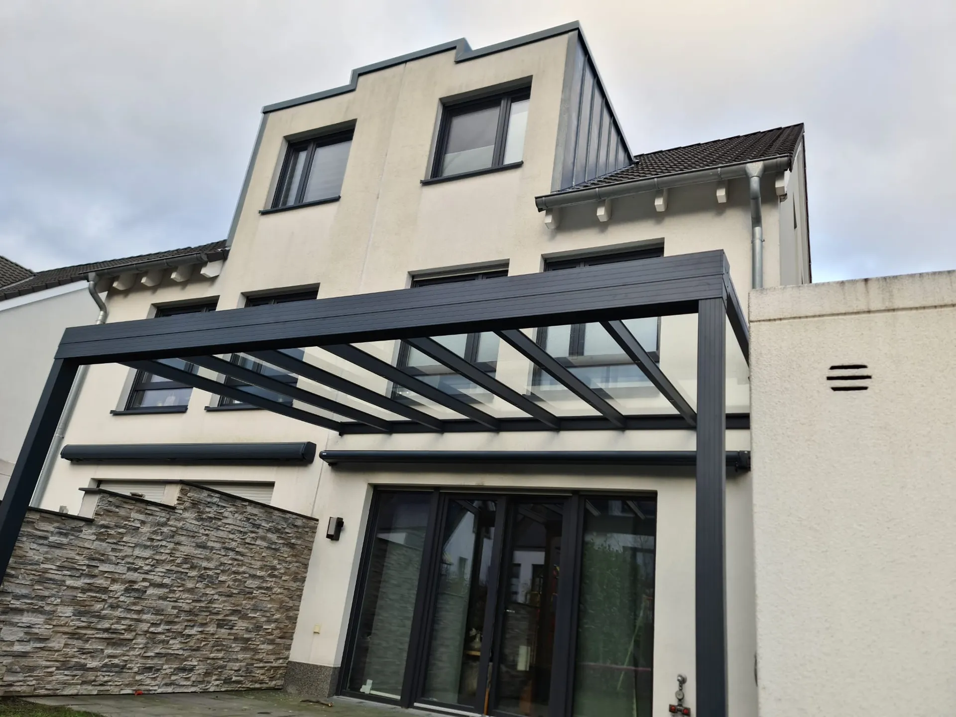 Moderne Terrassenüberdachung aus Aluminium mit Glasdach an Einfamilienhaus