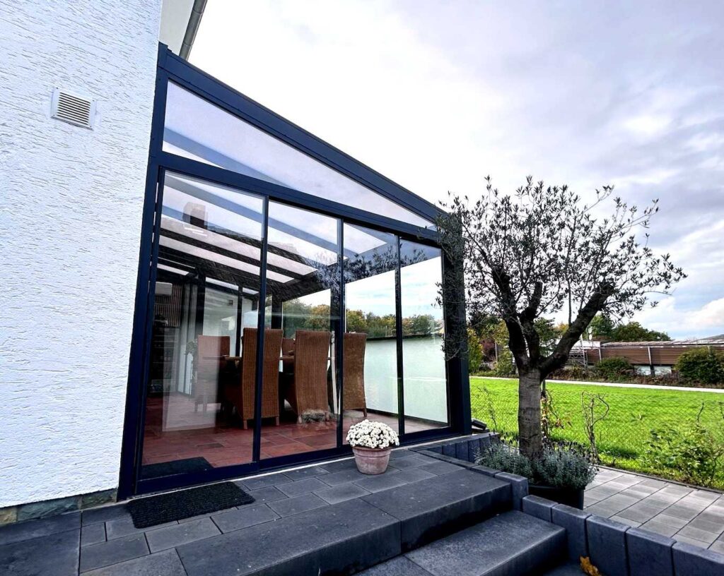 Terrassenüberdachung mit Glasdach und seitlichen Glasschiebewänden am Haus