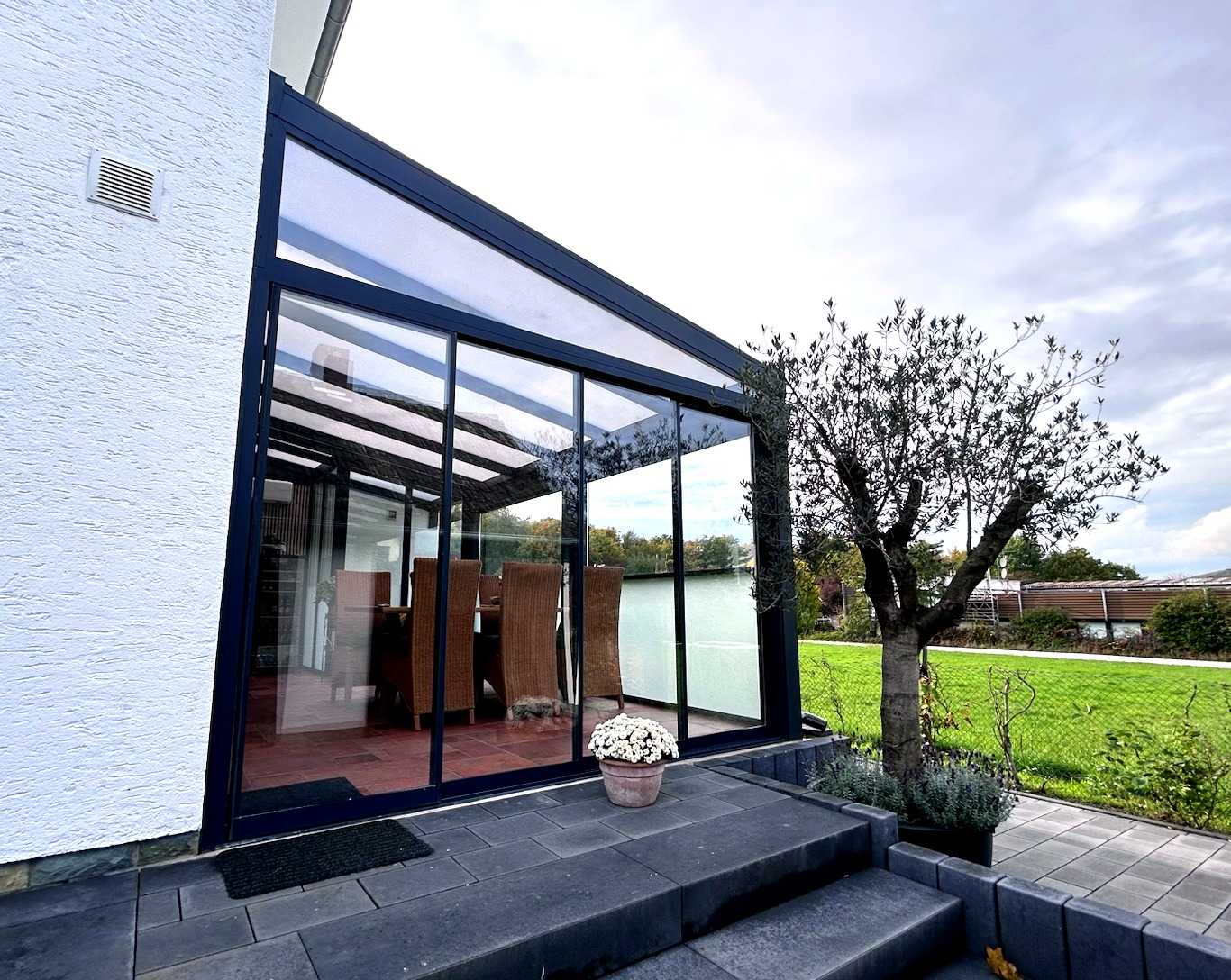 Terrassenüberdachung mit Glasdach und seitlichen Glasschiebewänden am Haus