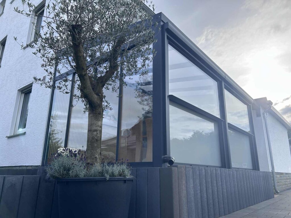 Moderne Terrassenüberdachung mit Glaswänden und Aluminiumrahmen im Garten