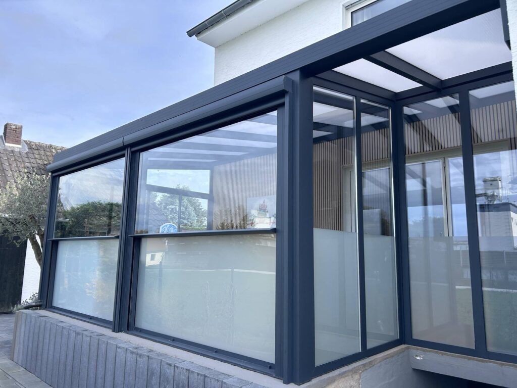 Moderne Terrassenüberdachung mit Glaswänden und teilweise satiniertem Glas an einem Wohnhaus