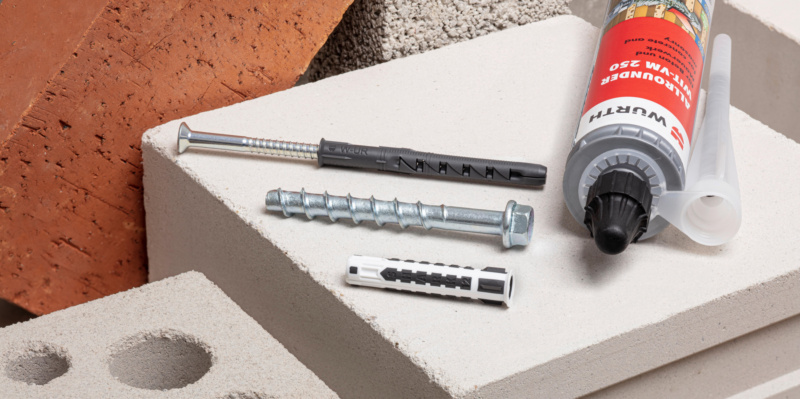 Verschiedene Befestigungsmaterialien wie Schrauben, Dübel und Injektionsmörtel auf Porenbetonstein